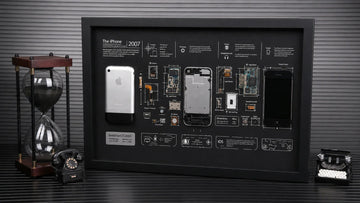 Black-framed iPhone teardown artwork displayed with vintage desk objects